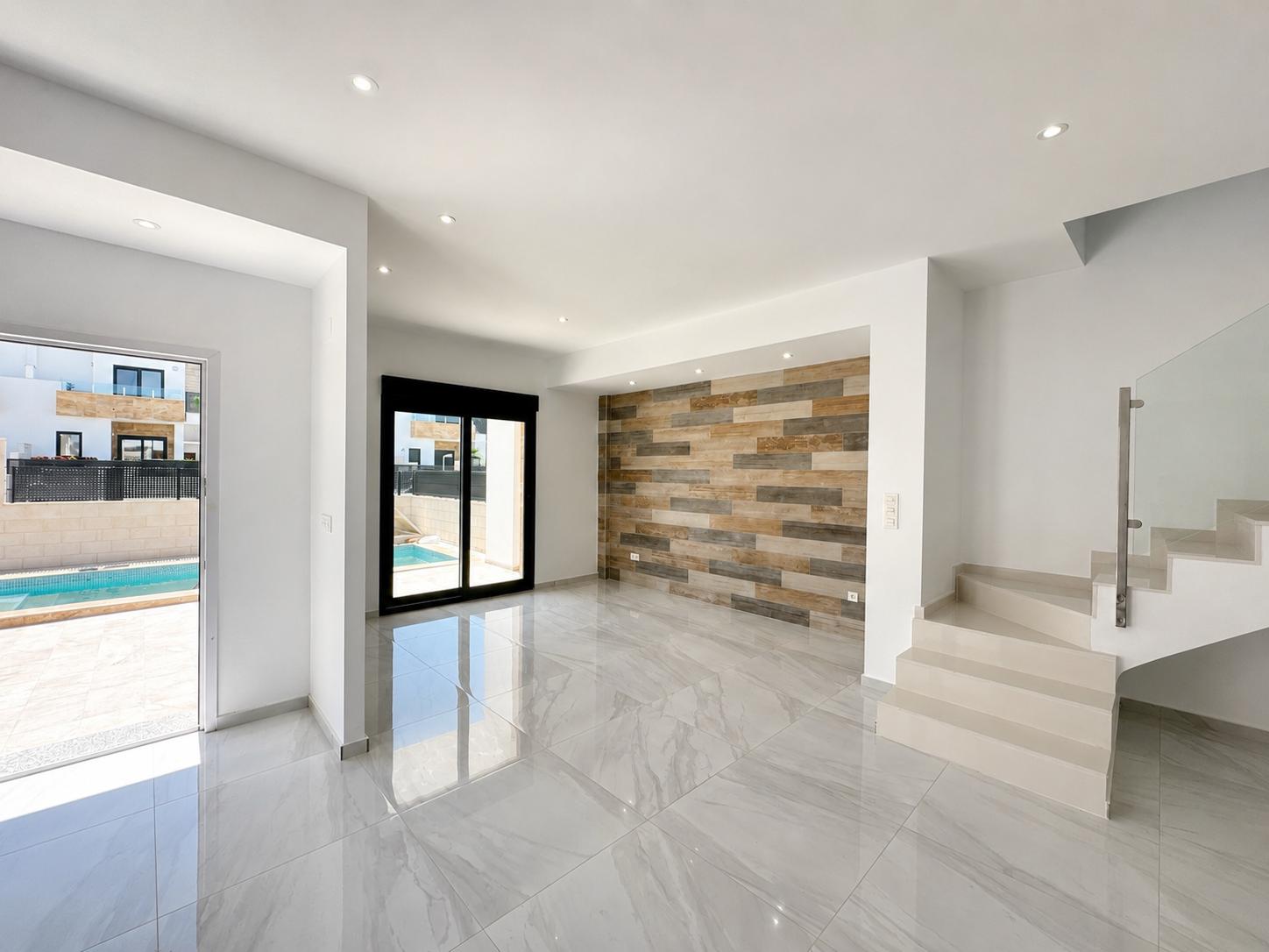 Ruime woonkamer met gepolijste porseleinen tegels, een decoratieve wand met houtlookpanelen en directe toegang tot het privézwembad. Moderne trap met glazen balustrade.