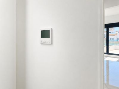Een strak digitaal klimaatregelpaneel is gemonteerd op een smetteloze witte muur, met een doorkijk naar een lichte aangrenzende kamer en buitenterras.