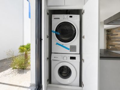 Geïntegreerde wasmachine en droger in wit meubilair, met directe toegang tot een aangelegd buitenpatio. Op de achtergrond is een moderne keuken met houten wandbekleding en donker aanrechtblad zichtbaar.