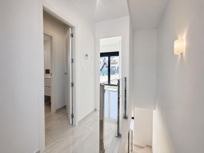 Lichte bovenverdieping hal met gepolijste marmerlook vloertegels en moderne glazen en stalen trapleuning. Een deur leidt naar een badkamer, een andere naar een buitenbalkon met daglicht.
