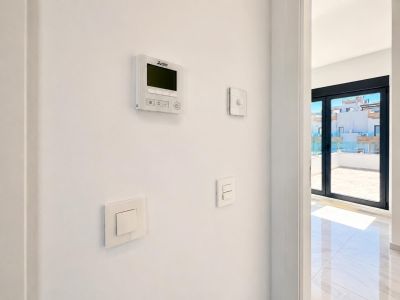 Mitsubishi airconditioning bedieningspaneel en moderne schakelaars op een witte muur, naast grote schuifdeuren die leiden naar een betegeld terras met glazen balustrade.