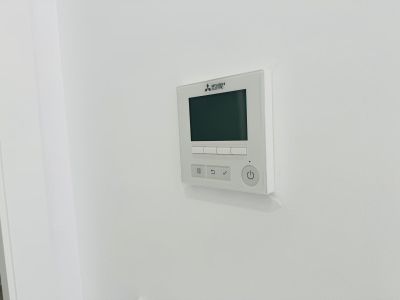 Mitsubishi Electric bedieningspaneel voor kanaalairconditioning, met digitaal display en intuïtieve knoppen, naadloos geïntegreerd in de witte muur.