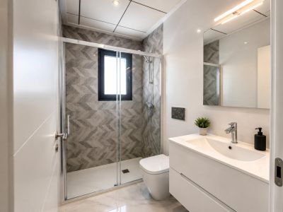 Moderne badkamer met inloopdouche, glazen wand, grijze geometrische wandtegels en raam. Witte zwevende wastafelmeubel op marmerlook vloer.
