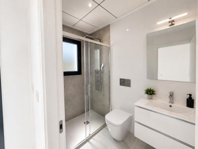 Moderne badkamer met zwevend wit wastafelmeubel, wandcloset en inloopdouche met grijze tegels en matglazen raam. Marmerlook vloertegels maken het strakke ontwerp compleet.
