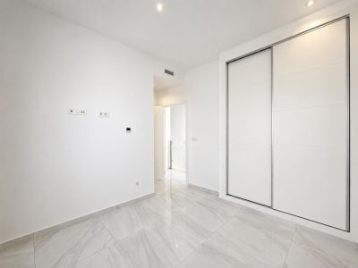 Moderne kamer met grote witte inbouwschuifkasten, lichtgrijze marmerlook vloertegels en inbouwspots. Een strak en functioneel ontwerp.