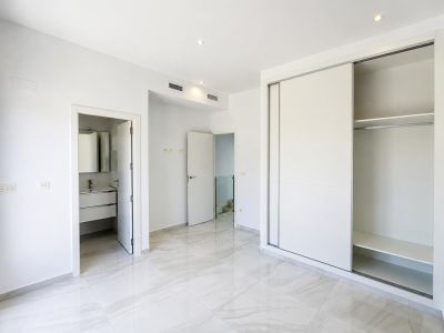 Ruime slaapkamer met lichte marmerlook tegelvloer, ingebouwde schuifdeurkast en directe toegang tot een moderne en-suite badkamer. Inbouwspots en airco-kanalen zijn zichtbaar.