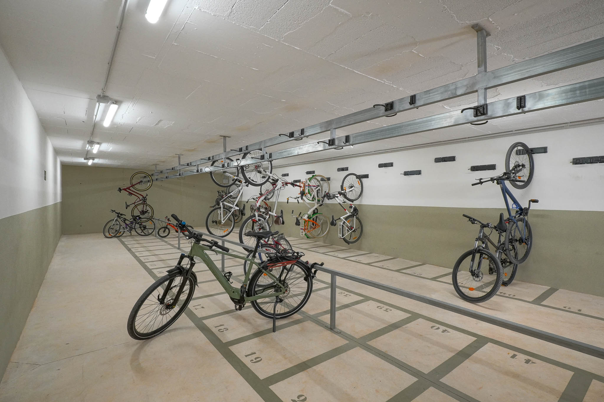 Ruime gemeenschappelijke fietsenstalling met genummerde vloerplaatsen en wandrekken. Helder verlicht door tl-buizen, biedt het veilige opslag binnen het wooncomplex.
