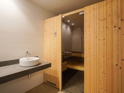 Kleedruimte met een strakke zwevende wastafel en opzetkom, naast de uitnodigende houten lamellen sauna-ingang met glazen paneel.
