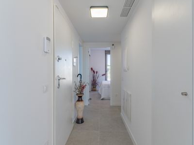 Lichte, moderne hal met lichtgrijze tegels en witte muren. Voorzien van een beveiligingspaneel, eigentijdse plafondverlichting en uitzicht op een slaapkamer.