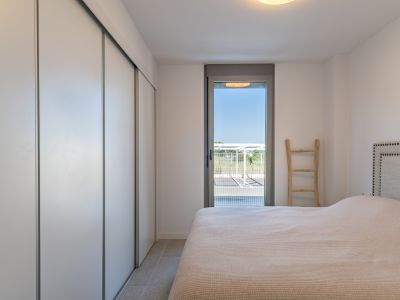 Lichte slaapkamer met ingebouwde kledingkast met witte schuifdeuren, tegelvloer en directe toegang tot de buitenruimte via een glazen deur. Bed met gestoffeerd hoofdbord.