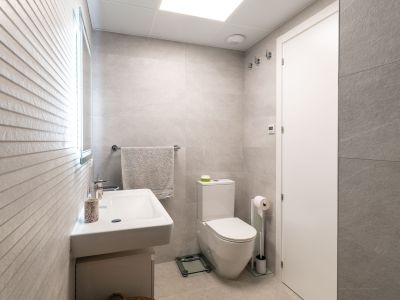 Moderne badkamer met lichtgrijze grootformaat tegels, een wandgemonteerde wastafel en toilet. De verlichte spiegel accentueert de getextureerde muur.