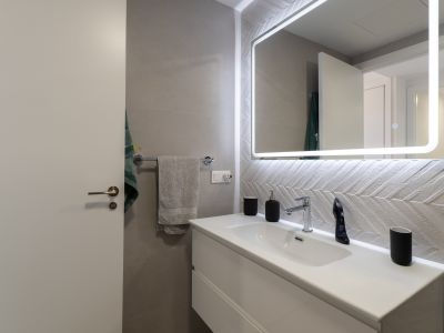Moderne badkamer met wit zwevend wastafelmeubel, chromen kraan en verlichte spiegel. Gekenmerkt door de getextureerde wandtegels met visgraatmotief.