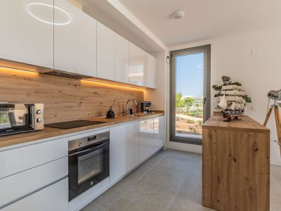 Moderne keuken met hoogglans witte kasten, houtlook werkblad en achterwand. Voorzien van geïntegreerde apparatuur, LED-verlichting en een raam met uitzicht op de tuin.