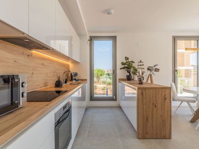 Moderne open keuken met glanzend witte kasten, werkbladen en spatwand in houtlook, en geïntegreerde apparatuur. Voorzien van LED-verlichting onder de bovenkasten en toegang tot buiten.