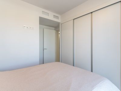 Slaapkamer met een ruime inbouwkast voorzien van witte schuifdeuren. De muur heeft moderne stopcontacten en geïntegreerde ventilatieroosters boven de aangrenzende deur.