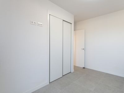 Slaapkamer met ruime inbouwkast voorzien van witte schuifdeuren en een lichtgrijze tegelvloer. Moderne stroom- en data-aansluitingen zijn aanwezig.