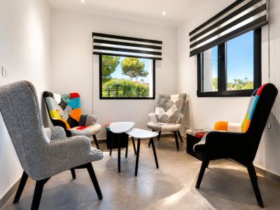 Gezellige zithoek met vier eclectische fauteuils en minimalistische bijzettafels. Ramen met gestreepte jaloezieën bieden natuurlijk licht en uitzicht op het groen.