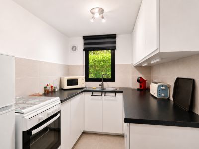 Moderne keuken met zwarte werkbladen, witte kasten en apparatuur, inclusief een spoelbak onder het raam met uitzicht op groen.
