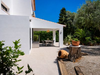 Ruime naya met lichte tegelvloer en eethoek buiten, geflankeerd door een mediterrane tuin met olijfboom en decoratieve elementen.