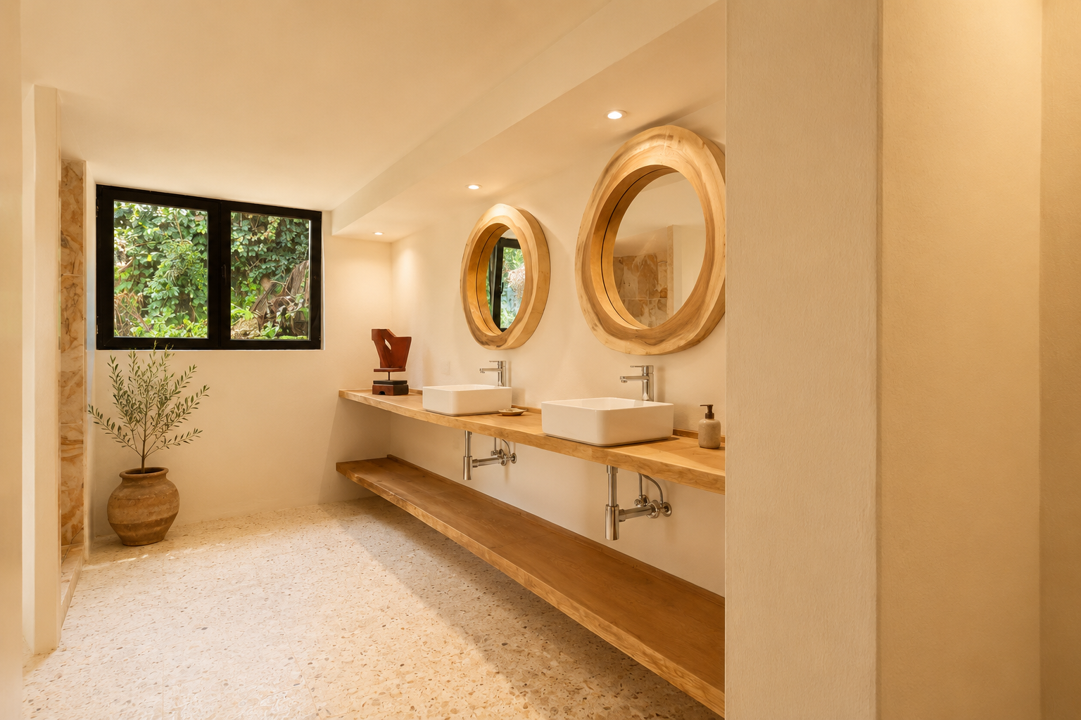 Badkamer met dubbele houten wastafel, twee witte rechthoekige waskommen en grote ronde spiegels met natuurlijke houten lijsten. Een raam biedt uitzicht op groen, passend bij de lichte terrazzovloer.