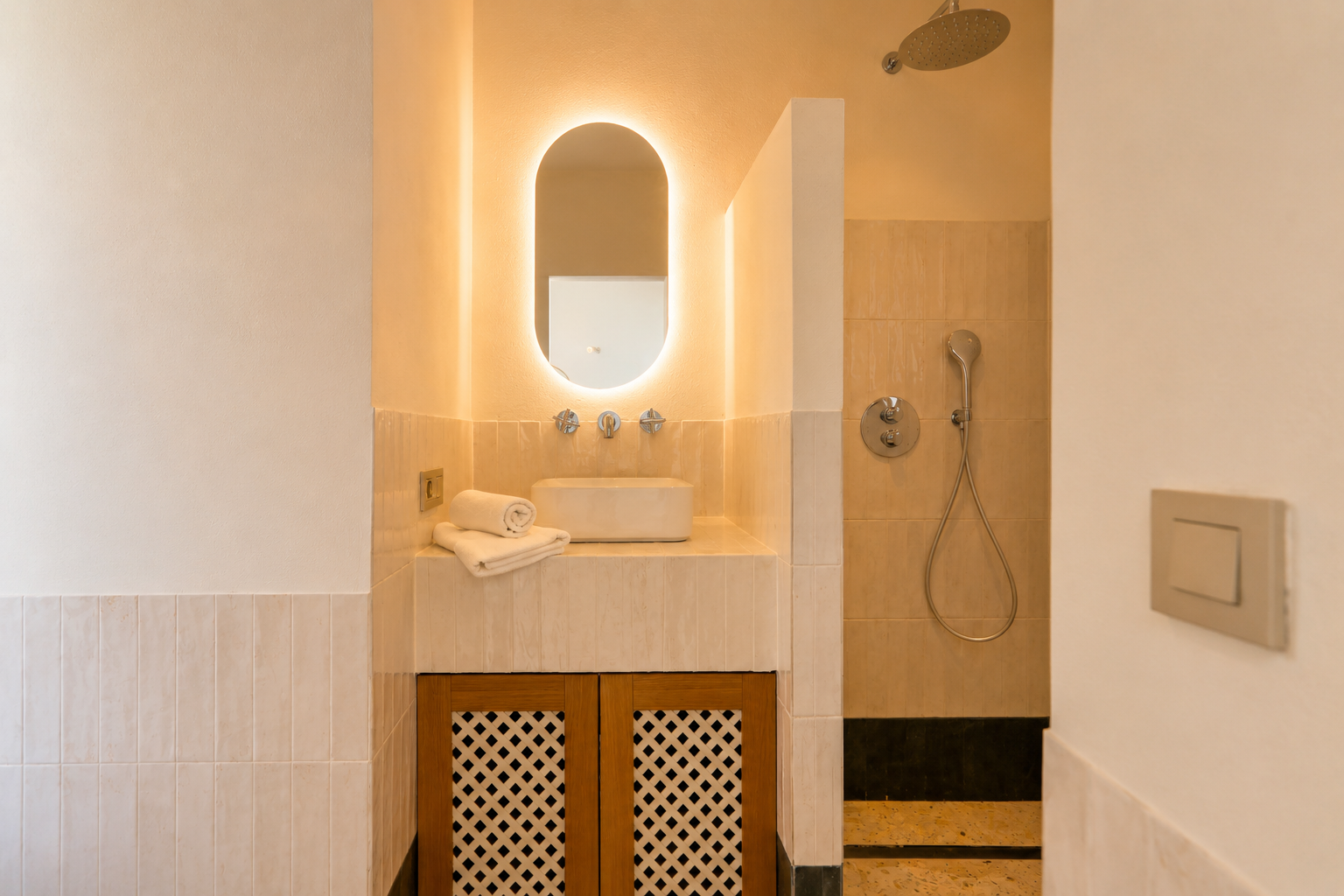 Deze elegante badkamer heeft een opbouw wastafel, een ovale spiegel met achtergrondverlichting en een houten kast met roosterdeuren. De douche heeft een regendouchekop.