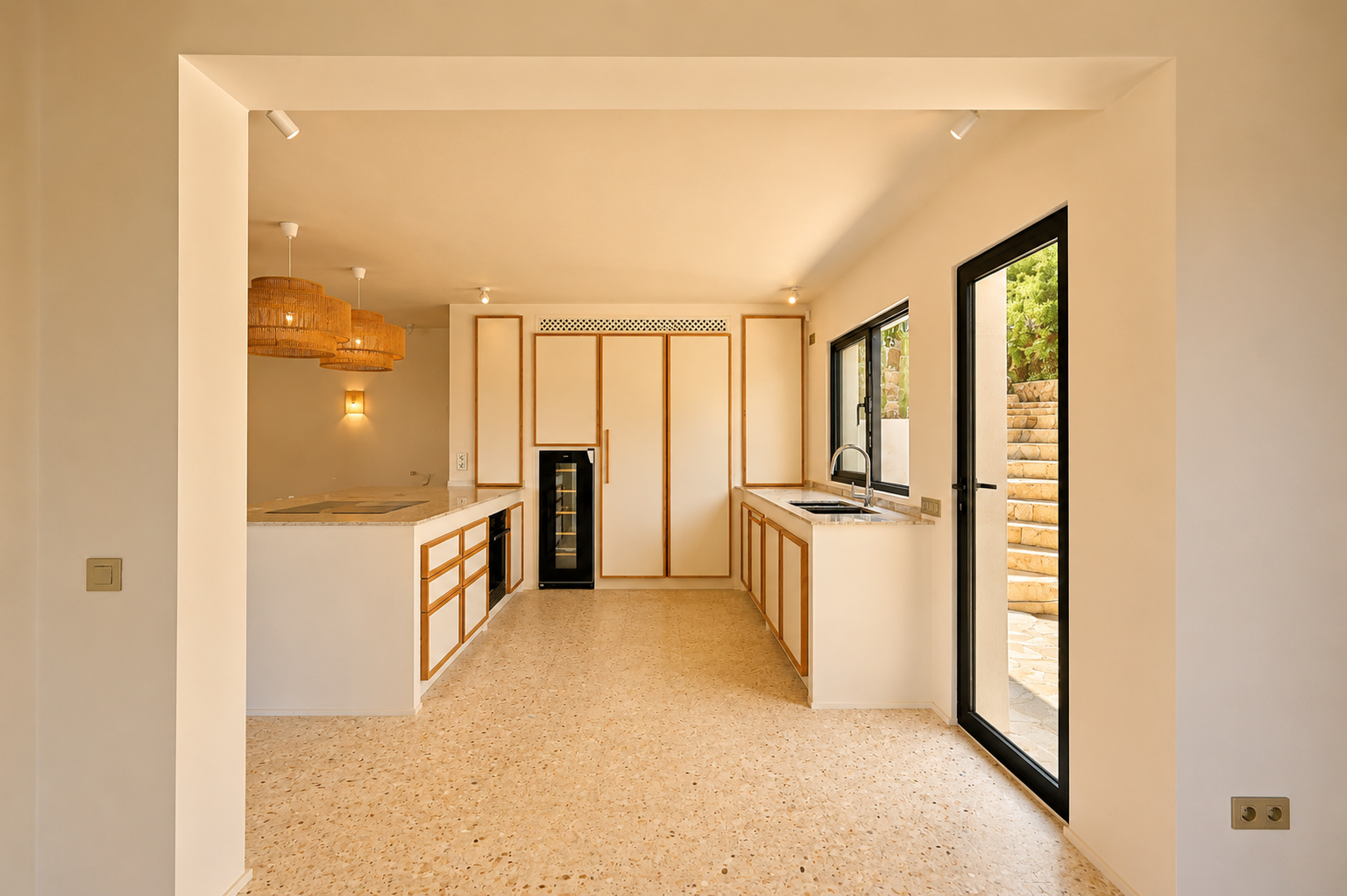 Moderne keuken met licht houten omrande kasten, terrazzostijl vloer en een groot kookeiland. Geweven hanglampen verlichten de ruimte.