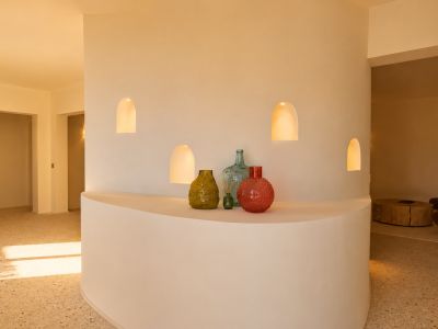 Gebogen scheidingswand met vier verlichte boognissen en een geïntegreerde plank met decoratieve vazen, op een terrazzovloer.