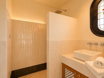 Moderne badkamer met inloopdouche, regendouchekop en indirecte LED-verlichting. Wastafel op tegelmeubel en een ovaal glas-in-loodraam met een roosmotief.