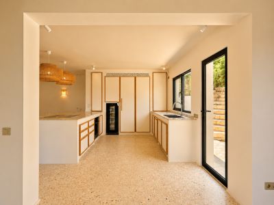 Moderne keuken met licht houten omrande kasten, terrazzostijl vloer en een groot kookeiland. Geweven hanglampen verlichten de ruimte.