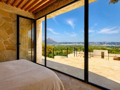 Slaapkamer met natuurstenen muren en houten balken, met directe toegang tot een terras met panoramisch uitzicht op de Montgó en de baai van Jávea.