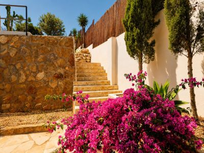 Stenen treden stijgen tussen een rustieke natuurstenen muur en een witte stucmuur, geflankeerd door een levendige bougainvillea en slanke cipressen.