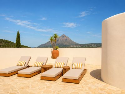 Terrassolarium met vier houten ligstoelen, gestreepte kussens, stenen bestrating en panoramisch uitzicht op de Montgó en de verre zee.