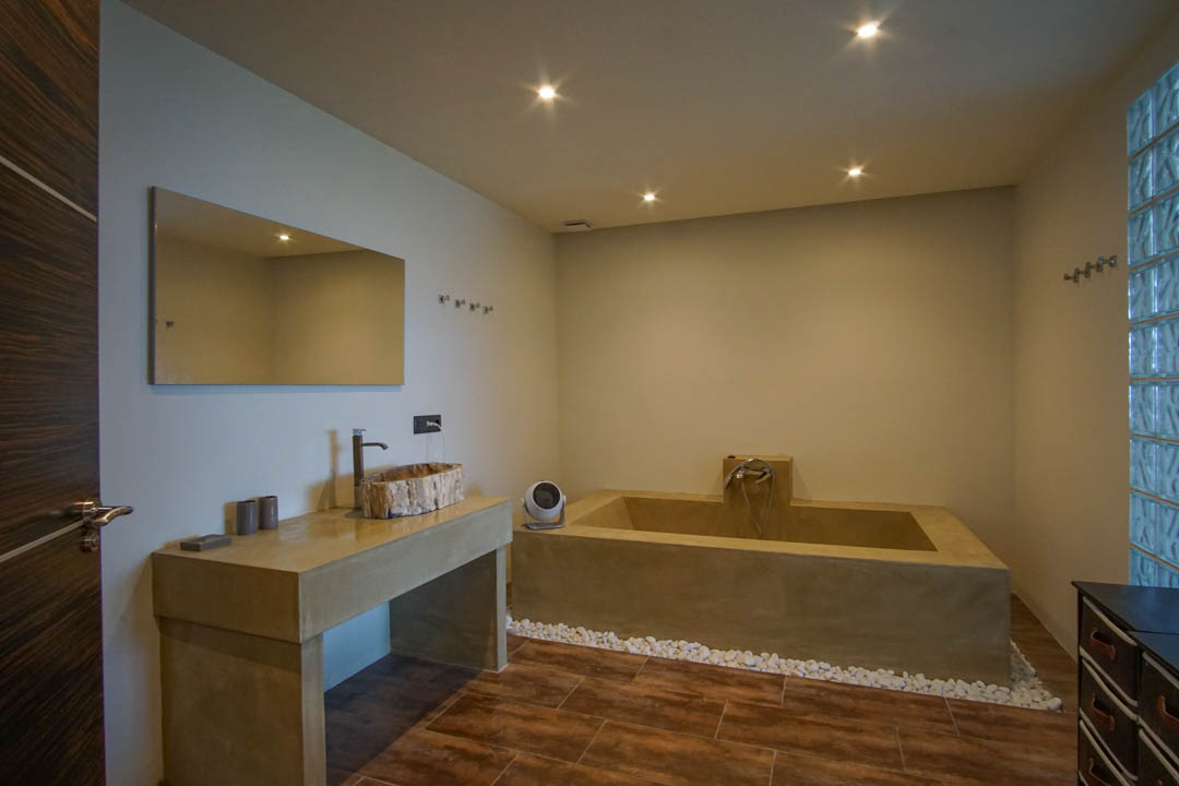 Moderne badkamer met unieke houten waskom op betonlook meubel, een ingebouwd bad en een glazen bouwstenenwand.