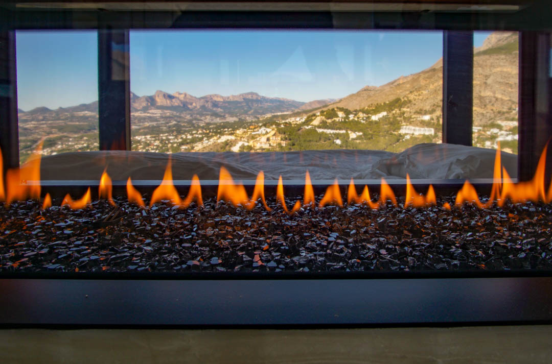 Moderne gashaard met vlammen op donker glasgranulaat, met panoramisch uitzicht op bergen en vallei.