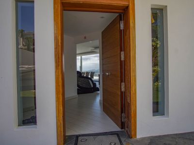 De open hoofdingang heeft een paneeldeur en kozijn van hout, geflankeerd door verticale ramen, en biedt een glimp van het moderne interieur met uitzicht op de bergen.