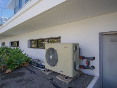 De technische buitenruimte van de villa omvat een AstralPool inverter warmtepomp, horizontale ramen en een technische deur. Agaveplanten sieren de moderne witte gevel.