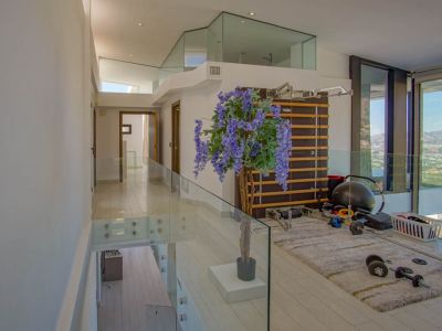 Fitnessruimte op de bovenverdieping met moderne glazen balustrades en lichte vloer. Voorzien van een rekstok en gewichten, biedt het panoramisch uitzicht door kamerhoge ramen.