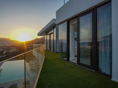 Het ruime terras met overloopzwembad, houten vlonder en glazen balustrade biedt panoramisch uitzicht op de zonsondergang over bergen en vallei.