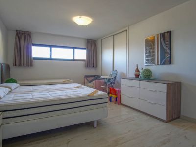 Lichte slaapkamer met een bed van twee matrassen, een lichte houtlook vloer en een langwerpig horizontaal raam. De kamer omvat een witte schuifdeurkast en een moderne ladekast met abstracte kunst erboven.