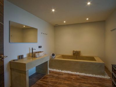 Moderne badkamer met unieke houten waskom op betonlook meubel, een ingebouwd bad en een glazen bouwstenenwand.