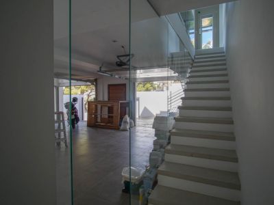 Moderne binnentrap met glazen balustrade en lichte treden, grenzend aan een betegelde garage met open deur en natuurlijk daglicht.