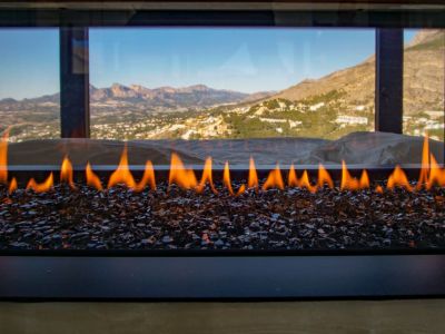 Moderne gashaard met vlammen op donker glasgranulaat, met panoramisch uitzicht op bergen en vallei.