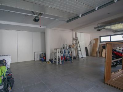 Ruime garage met grijze tegelvloer en witte muren. Voorzien van twee automatische poortmechanismen, horizontale ramen en witte schuifdeuren voor opslag.