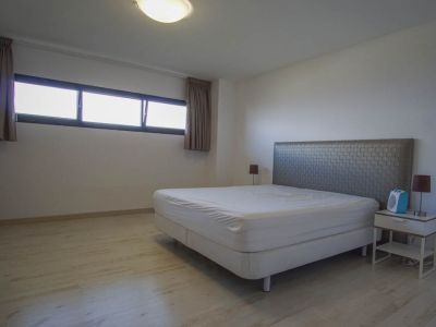 Slaapkamer met lichte houtnerf vloer en witte muren. Voorzien van een bed met gestructureerd hoofdbord, nachtkastje en een langwerpig raam met donkere kozijnen.