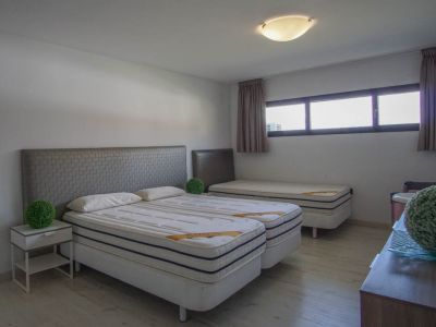 Slaapkamer met twee samengevoegde eenpersoonsbedden, grijze gestructureerde hoofdeinden, een derde eenpersoonsbed achterin, lichte houten vloer en horizontale ramen.