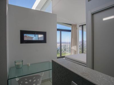 Studeerhoek met glazen bureau en horizontaal raam, dat panoramisch zee- en stadszicht biedt vanuit de aangrenzende slaapkamer.