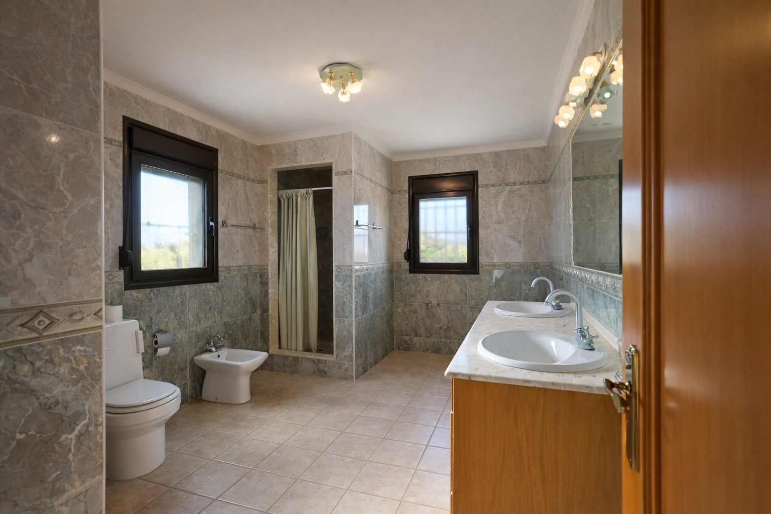 Ruime badkamer met dubbele wastafel op marmeren blad en houten onderkast. Voorzien van inloopdouche, toilet, bidet en twee ramen die natuurlijk licht binnenlaten.