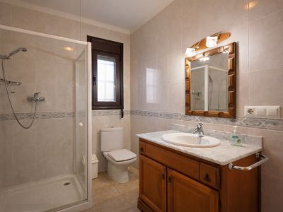 Badkamer met inloopdouche, toilet en een houten badmeubel met marmeren blad. De wanden zijn betegeld met lichte tegels en een decoratieve rand.