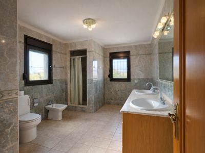 Ruime badkamer met dubbele wastafel op marmeren blad en houten onderkast. Voorzien van inloopdouche, toilet, bidet en twee ramen die natuurlijk licht binnenlaten.