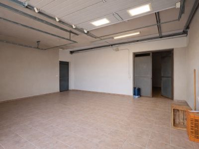 Ruime garage of technische ruimte met lichte tegelvloer, industriële plafondverlichting en meerdere toegangspunten.